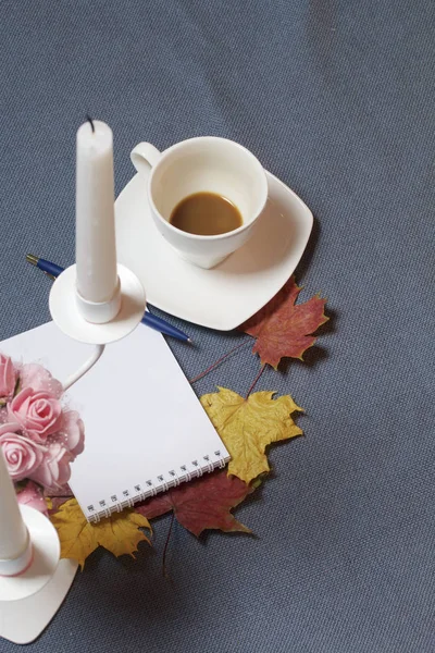 Bougeoir en métal forgé avec bougies. Il y a un bloc-notes ouvert et un stylo. Une tasse avec du café non approuvé. Les feuilles tombées en automne de jaune et de rouge sont éparpillées à la surface . — Photo