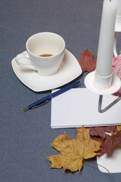 Bougeoir en métal forgé avec bougies. Il y a un bloc-notes ouvert et un stylo. Une tasse avec du café non approuvé. Les feuilles tombées en automne de jaune et de rouge sont éparpillées à la surface . — Photo