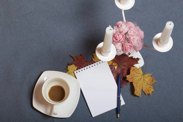 Bougeoir en métal forgé avec bougies. Il y a un bloc-notes ouvert et un stylo. Une tasse avec du café non approuvé. Les feuilles tombées en automne de jaune et de rouge sont éparpillées à la surface . — Photo