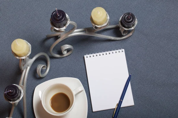 Bougeoir en métal forgé avec bougies. Une tasse avec du café non approuvé. Il y a un bloc-notes ouvert et un stylo. Les feuilles tombées en automne de jaune et de rouge sont éparpillées à la surface . — Photo