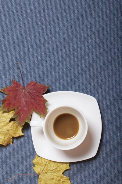 Pohár s neschválené kávy. Podzimní listí žluté a červené jsou roztroušeny na povrchu. — Stock fotografie