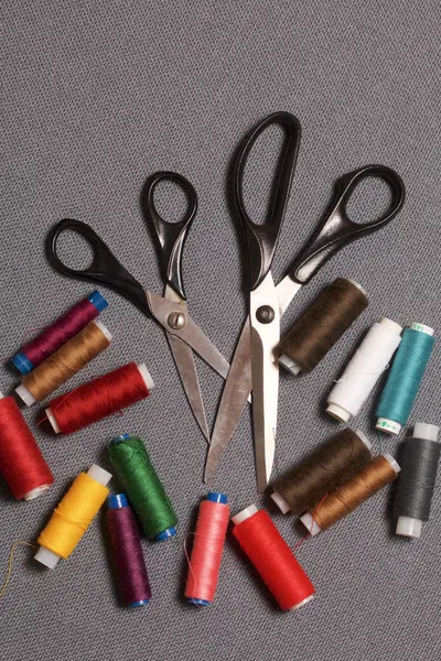 Špulka na nití různých barev na šedé tkané pozadí. Dvoje nůžky různých velikostí. — Stock fotografie