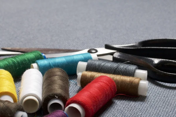 Coils of thread of different colors on a gray fabric background and scissors. — Stock Photo, Image