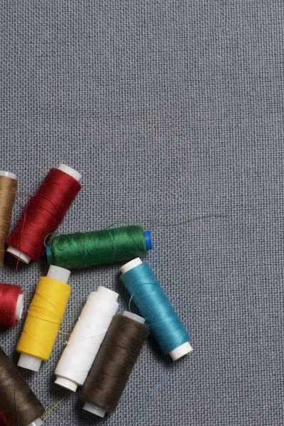 Cívek nití různých barev na šedé tkané pozadí — Stock fotografie