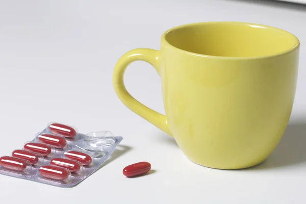 Blister con píldoras rojas. Faltan varias pastillas. Cerca hay una taza con agua y una pastilla para el uso . —  Fotos de Stock