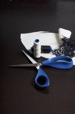 Dikiş ve sos. Karanlık bir yüzeye makas, iplik makaraları ve süsleme kumaş yalan