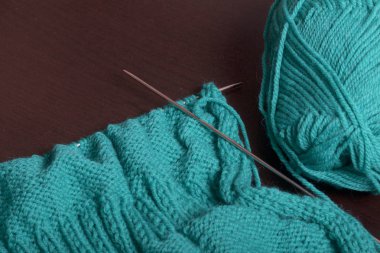 Örgü örgü iğne ile. Örgü iğne ve Zümrüt renginde konu bir top ile bitmemiş bir örme ürün tablo karanlık yüzeyinin üzerinde yatıyor.