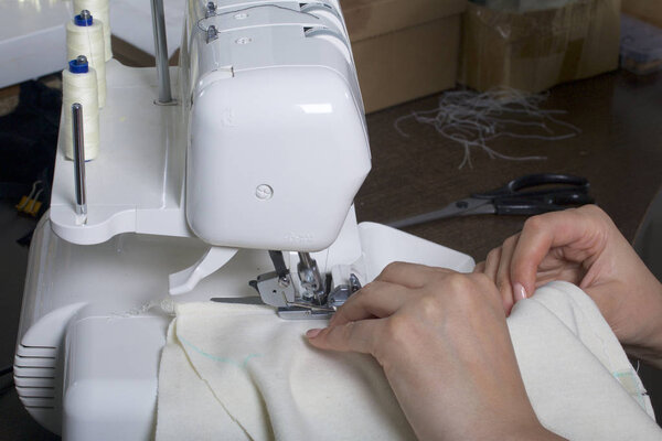 The woman is working on the product on the overlock. Overlock with white thread. The woman directs the cloth clamped in the claw of the overlock.