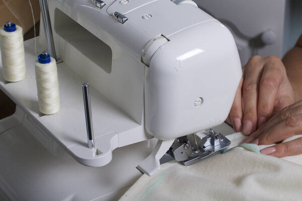 The woman is working on the product on the overlock. Overlock with white thread. The woman directs the cloth clamped in the claw of the overlock.
