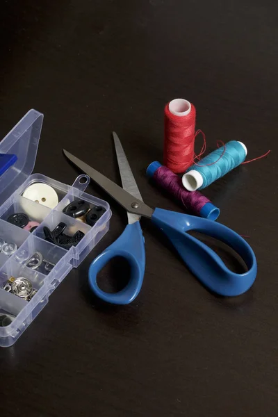 Sur la surface de la table se trouve une boîte avec des accessoires de couture. À côté de quelques bobines de fil et de ciseaux . — Photo