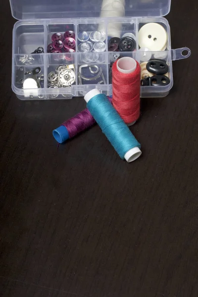On the surface of the table is a box with sewing accessories. Several coils of thread lie next to each other. — Stock Photo, Image