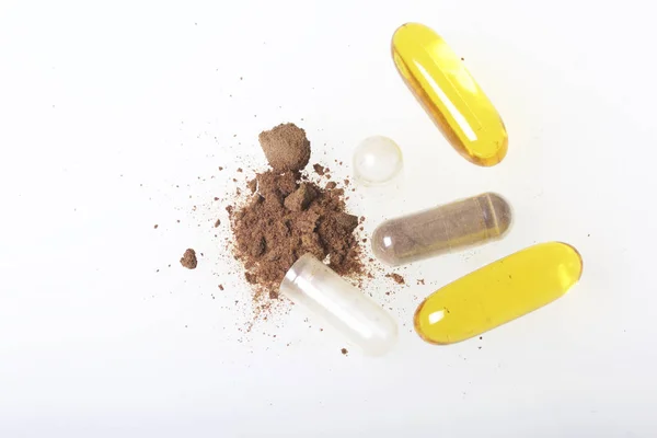 Las pastillas marrones están esparcidas por la superficie blanca. Un ingrediente activo se vierte a partir de una pastilla. Vista desde arriba . —  Fotos de Stock