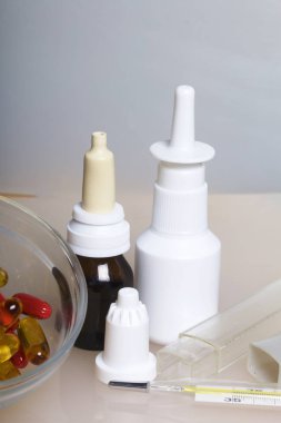 Burun damlası, sprey ve hapları bir cam kap içinde ayağa yüzeyde. Vücut ısısını ölçmek için bir termometre yakın olduğunu.