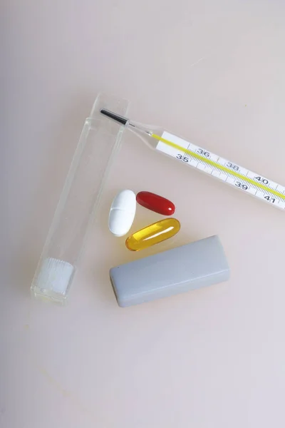 Medicinale pillen van verschillende kleuren op het oppervlak liggen. In de buurt is een thermometer voor het meten van de lichaamstemperatuur. — Stockfoto