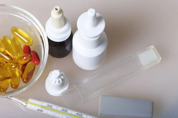 Nasal drops, spray and pills in a glass container, stand on the surface. Nearby is a thermometer for measuring body temperature. — Stock Photo, Image