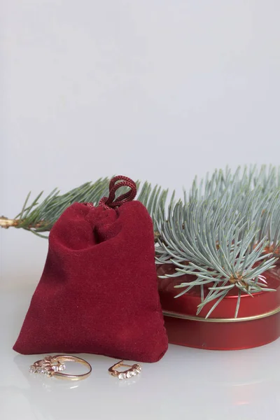 Un regalo para un ser querido. Una bolsa roja de terciopelo y una caja de regalo en forma de corazón. Muy cerca hay un anillo de oro y pendientes de oro. Sobre un fondo blanco con una rama de abeto . —  Fotos de Stock