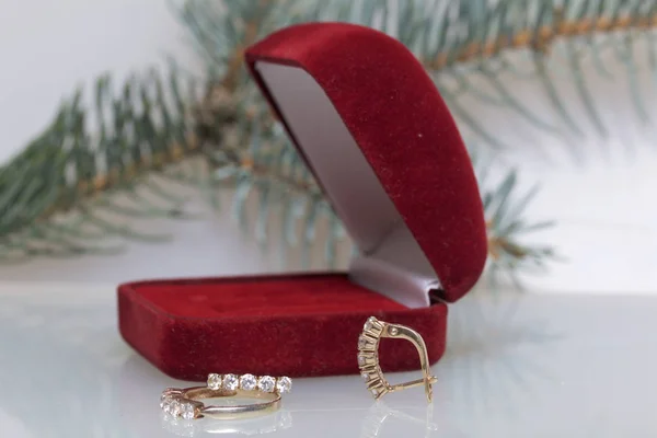 Ein Geschenk an einen geliebten Menschen. eine offene Samtbox mit roter Farbe und goldenen Ohrringen. In der Nähe befindet sich ein goldener Ring. auf weißem Hintergrund mit einem Fichtenzweig. — Stockfoto