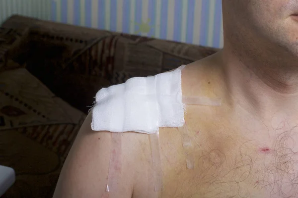 A man with a collarbone injury. The surgical suture is covered with a gauze swab and fixed with a plaster adhesive.