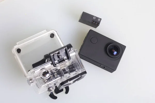 La caméra d'action repose sur une surface blanche. Près de la boîte pour la prise de vue sous-marine et une batterie de rechange. Vue d'en haut . — Photo