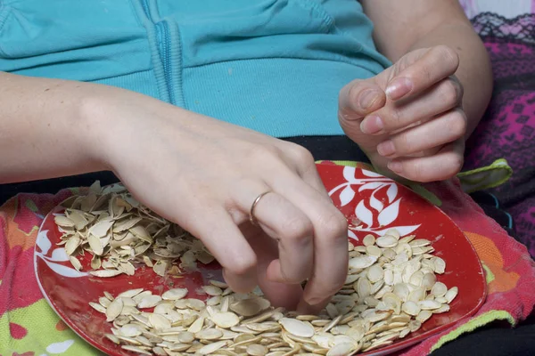 Fata mănâncă seminţe de dovleac. Semințele se află pe o farfurie, lângă ea se află coji . — Fotografie, imagine de stoc