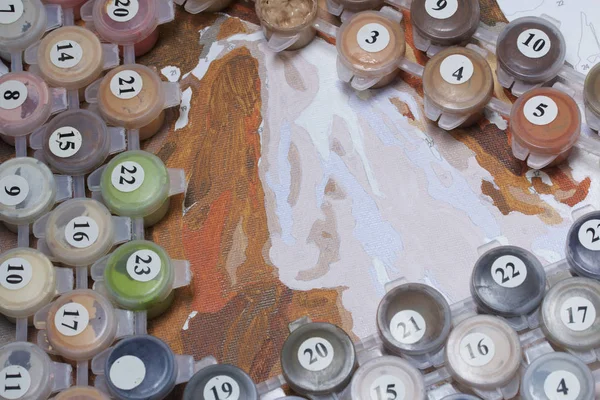 Painting on canvas by numbers. Numbered containers with paints and brushes lie on the canvas background.