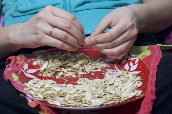 The girl is eating pumpkin seeds. Seeds lie on a plate, next to it lies the husks. — Stock Photo, Image