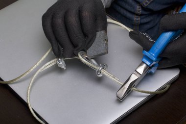 Bilgisayar güvenliği. Verilere erişimin korunması. Belgili tanımlık laptop bir güvenlik kablosu ve bir kilit tarafından korunmaktadır. Kilidi açmak ve bilgisayara erişmek bir saldırgan eldiven ile çalışır.