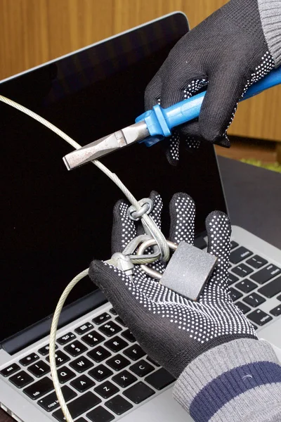 Computer security. Protection of access to data. The laptop is protected by a security cable and a lock. An attacker with gloves tries to open the lock and get access to the computer.