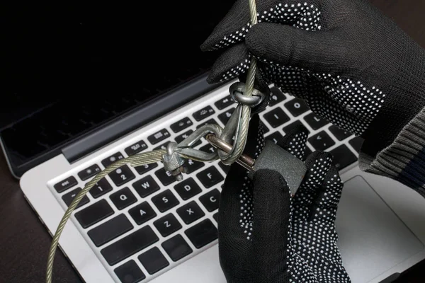 Computer security. Protection of access to data. The laptop is protected by a security cable and a lock. An attacker with gloves tries to open the lock and get access to the computer.