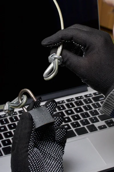 Zabezpieczenia komputera. Ochrona dostępu do danych. Laptop jest chroniony przez kabel zabezpieczenia i blokady. Osoba atakująca z rękawice próbuje otworzyć zamek i uzyskać dostęp do komputera. — Zdjęcie stockowe