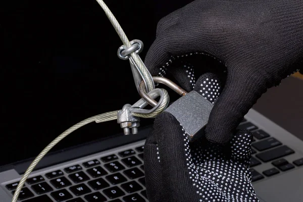 Sicurezza informatica. Protezione dell'accesso ai dati. Il computer portatile è protetto da un cavo di sicurezza e una serratura. Un aggressore con i guanti cerca di aprire la serratura e accedere al computer . — Foto Stock