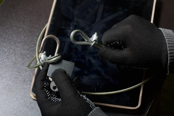 Computer security. Protection of access to data. The tablet is protected by a security cable and a lock. An attacker with gloves tries to open the lock and get access to the computer.