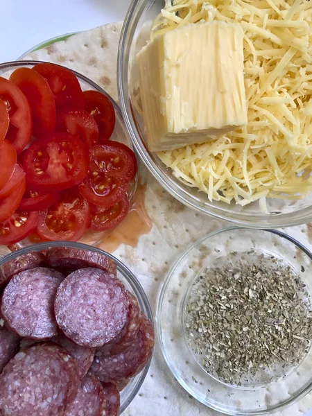 Pizza hazırlık. Gerekli malzemeler masada vardır: peynir, sosis, pizza tabanı ve sebze. — Stok fotoğraf