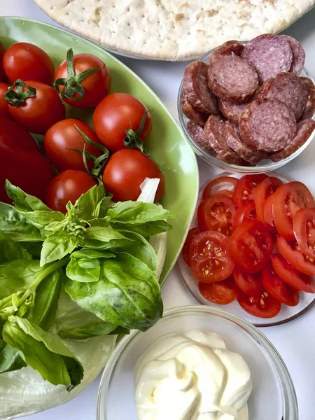 Příprava pizzy. Na stole jsou potřebné ingredience: sýr, klobása, pizza základny a zeleniny. — Stock fotografie