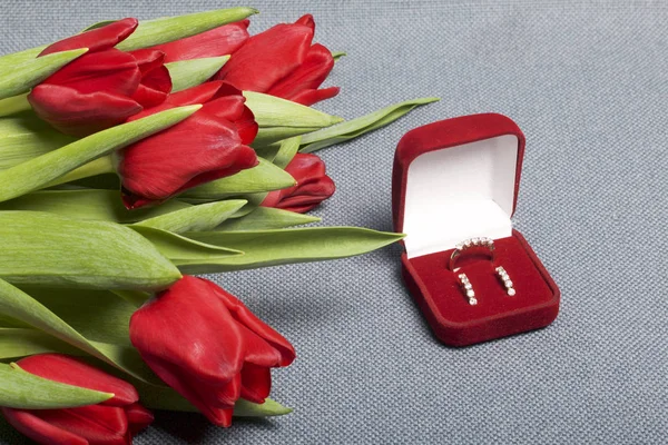 Presentes para entes queridos. Um buquê de tulipas vermelhas. Nas proximidades é uma caixa de veludo vermelho com um anel e brincos . — Fotografia de Stock
