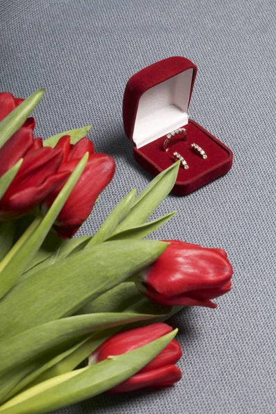 Presentes para entes queridos. Um buquê de tulipas vermelhas. Nas proximidades é uma caixa de veludo vermelho com um anel e brincos . — Fotografia de Stock
