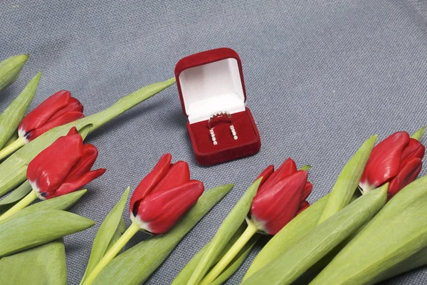 Geschenke für geliebte Menschen. ein Strauß roter Tulpen. In der Nähe befindet sich eine rote Samtbox mit einem Ring und Ohrringen. — Stockfoto