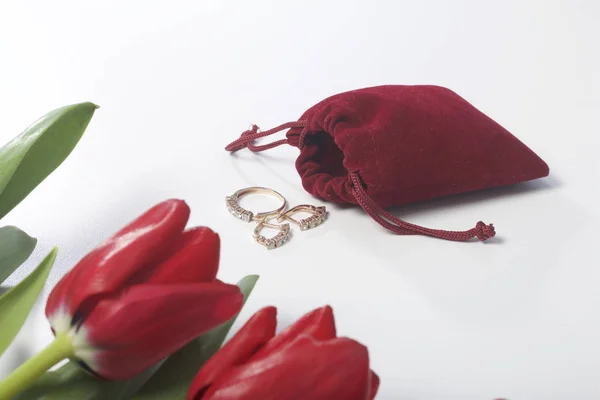 Ajándékot szeretteinek. Egy csokor piros tulipán szóródott a fehér felület. A közelben van egy piros bársony táska-val egy gyűrű és fülbevaló. — Stock Fotó