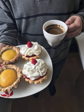 Bir fincan kahve ve kek bir tabak genç bir adam tutar.