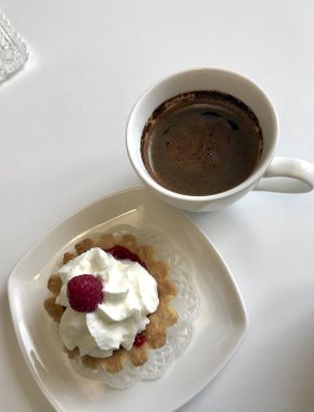 Bir fincan kahve, bir ahududu meyveleri ve kek masaya vardır.