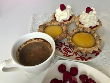 Bir fincan kahve, bir ahududu meyveleri ve kek masaya vardır.