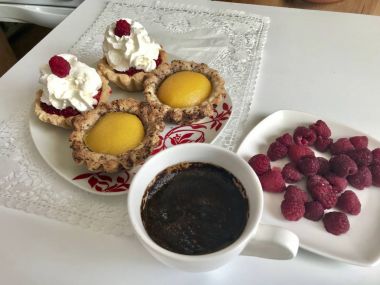 Bir fincan kahve, bir ahududu meyveleri ve kek masaya vardır.