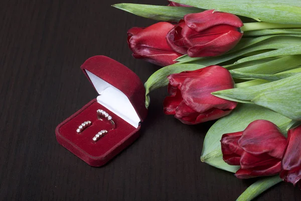 Gifts for loved ones. A bouquet of red tulips. Nearby is a red velvet box with a ring and earrings. — Stock Photo, Image