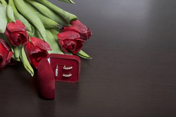 Dárky pro blízké. Kytice červených tulipánů. Nedaleko je krabice červeného sametu s prsten a náušnice. — Stock fotografie