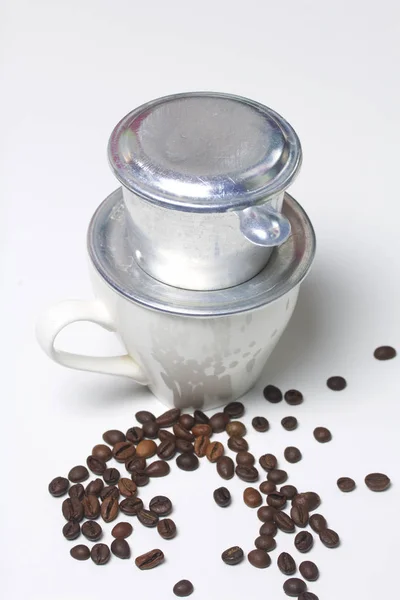 Der vietnamesische Kaffeebrauer in zusammengebauter Form steht auf einer weißen Tasse. nächste verstreute Kaffeebohnen. — Stockfoto