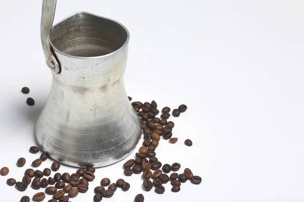 Cezve de pie sobre una superficie blanca. Siguiente granos de café dispersos . — Foto de Stock