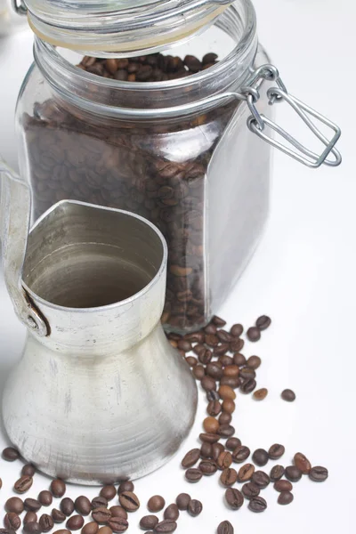 Cezve se tient sur une surface blanche. À côté d'un bocal en verre avec grains de café . — Photo