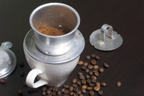 Vietnamese coffee maker is equipped on a cup. Ground coffee is poured into it. Nearby lie the rest of the brewer.