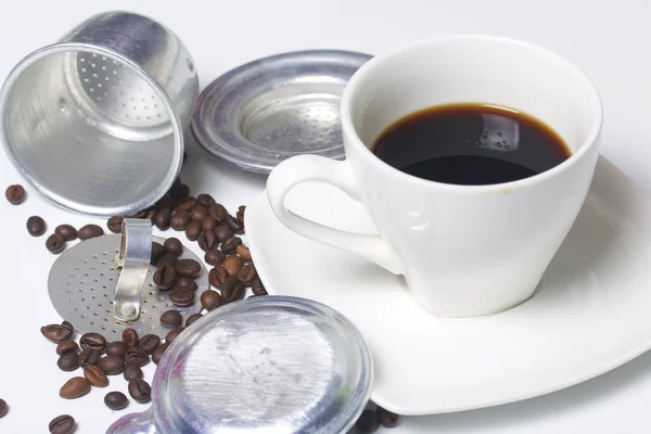 Una taza de café está en el platillo. La tetera vietnamita para el café en forma desmontada se encuentra en una superficie. Siguiente granos de café dispersos . — Foto de Stock