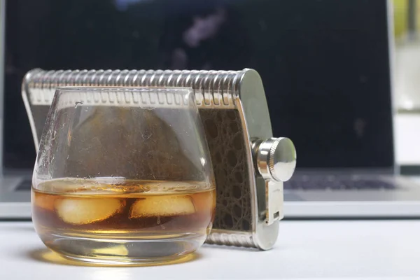 Whiskey with ice in a glass and a flask. Nearby is a laptop. Rest of the day off. — Stock Photo, Image
